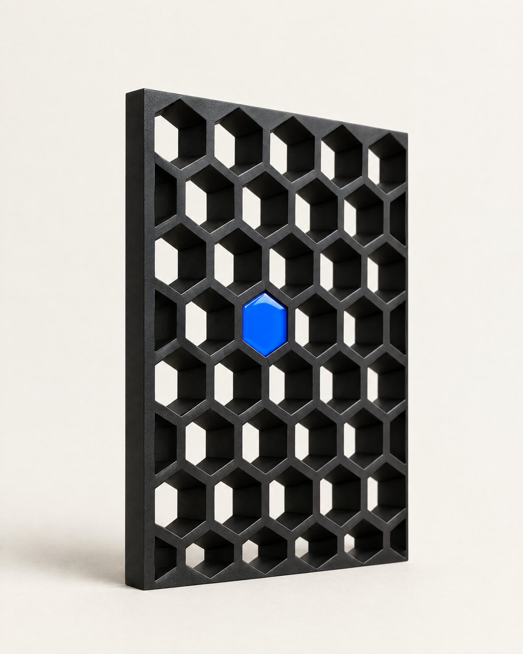 Machined black honeycomb panel with one blue cell — studio still life