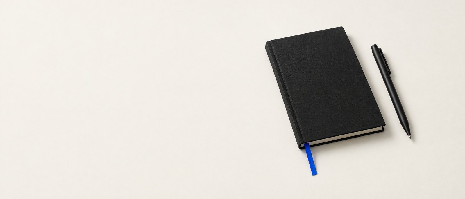 Black linen notebook with a blue ribbon and a machined pen — studio still life