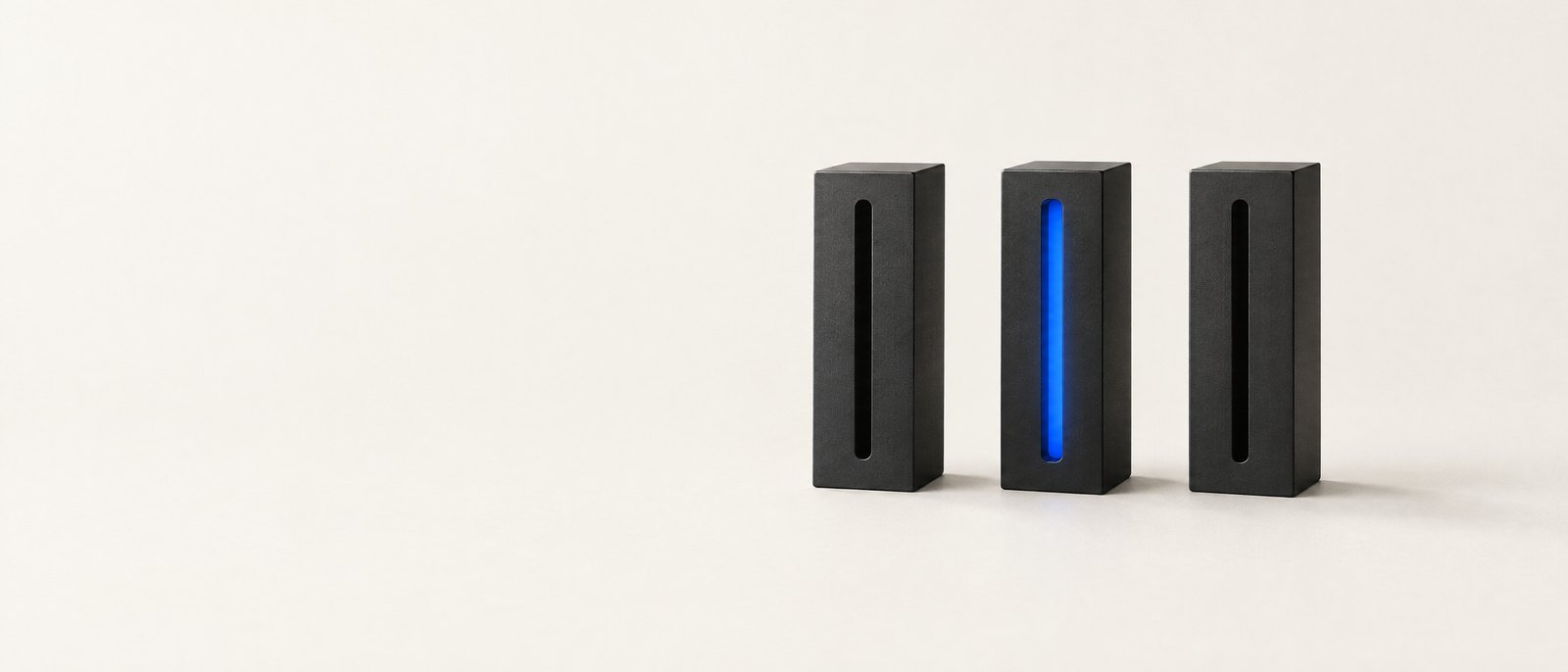Three black machined blocks with slots, the middle one lit blue — studio still life